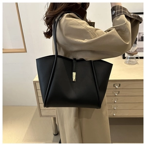 Borsa tote nera minimalista in ecopelle con fibbia dorata indossata da modella in trench coat