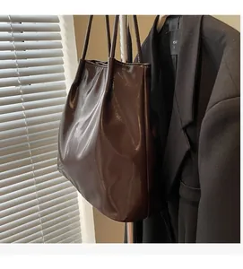 Detail of glossy deep brown tote bag hanging on a metal rack with sleek patent leather texture