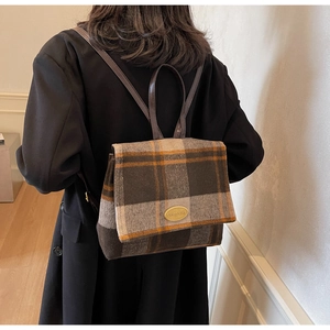 Détail d'un sac à dos en laine à carreaux avec logo métallique et fines lanières de cuir