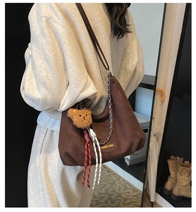Détail du sac hobo en daim marron foncé avec chaîne en métal et breloque ours
