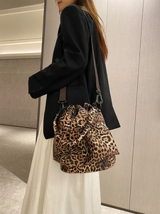 Detail of leopard print bucket bag with brown strap and drawstring closure shown on model
