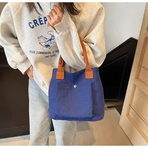 Détail du sac cabas en toile bleu marine avec anses marron et poche avant à bouton-pression