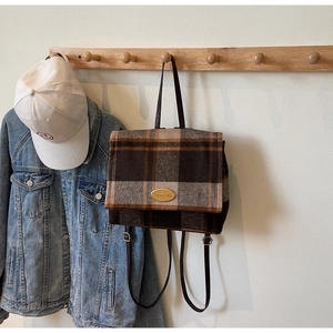 Détail d'un sac à dos vintage en laine à carreaux avec logo doré et fines bretelles en cuir