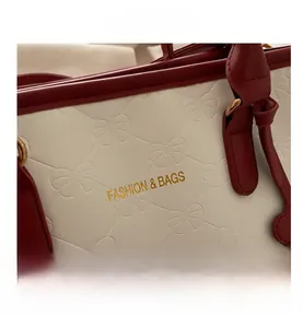 Detail of embossed bow texture on leather bag with gold lettering and red contrast trim