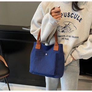 Détail du sac fourre-tout bleu en toile avec poignées marron et poche à bouton pression
