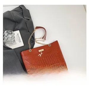 Detail of brown croc-embossed tote bag featuring gold chain strap and deer pendant