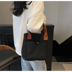 Détail du sac cabas en toile noire avec anses brunes et grande poche extérieure à bouton