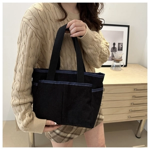Gros plan du sac cabas en velours côtelé noir avec poches et bordure bleue élégante