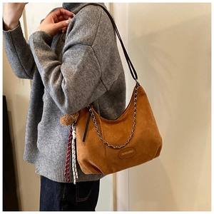 Détail du sac sous le bras en daim caramel avec chaîne argentée et breloque à franges