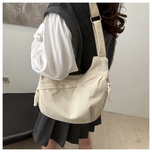 Vue verticale d'un grand sac bandoulière en velours côtelé crème porté par un mannequin