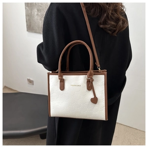 Detail showing white leather tote with bow patterns, brown trim and heart charm