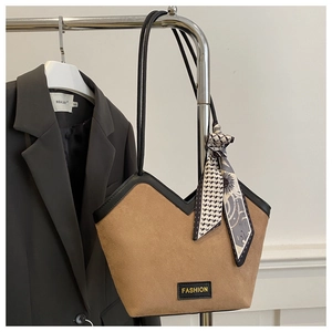 Detail of tan suede tote bag with V-cut edge, fashion label, and geometric scarf accessory