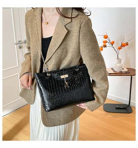 Detail of black faux crocodile leather shoulder bag with gold deer charm and chain strap
