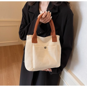 Détail du sac cabas en toile avec anses brunes et poche à pression porté par un mannequin