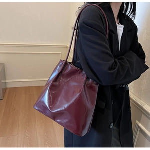 Detail of burgundy glossy pleated tote bag worn by a model in a minimalist studio setting
