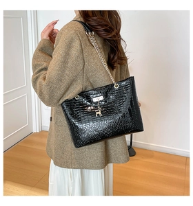 Detail of black faux-crocodile tote with gold chain strap and deer charm on a shoulder
