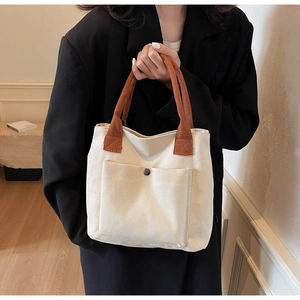 Détail du cabas en toile avec poche avant, bouton en métal et poignées brunes
