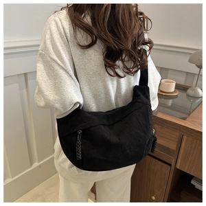 Détail d'un sac demi-lune en velours côtelé noir porté par un mannequin dans un décor intérieur