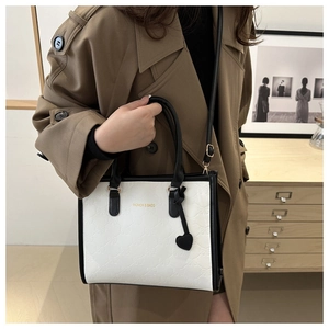 Detail of white leather tote featuring embossed bows and contrast black heart charm