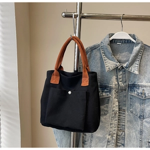 Détail du sac en toile noire avec anses brunes et bouton sur veste en jean bleu