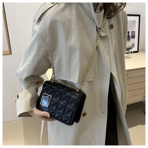 Détail du sac bandoulière matelassé noir avec chaîne dorée sur trench-coat beige