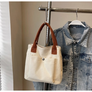 Détail d'un sac cabas en toile beige avec poche avant et poignée en textile brun