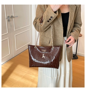 Detail of glossy brown croc-embossed tote bag featuring a gold deer charm on model