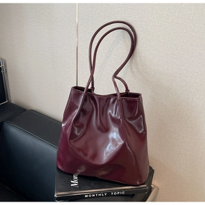Detail view of burgundy PU leather tote bag with slim shoulder straps on a sofa