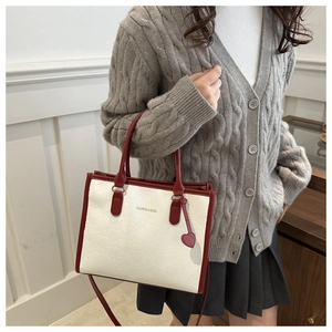 Detail of cream tote bag with red trim, heart pendant, and textured bow patterns