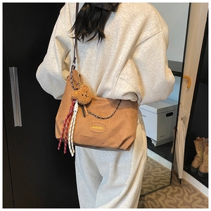 Détail du sac à bandoulière kaki avec breloque ours et étiquette de mode porté par un mannequin