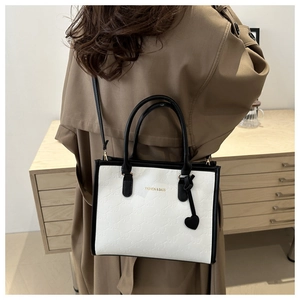Detail of contrast bow embossed tote bag with heart charm on a trench coat model