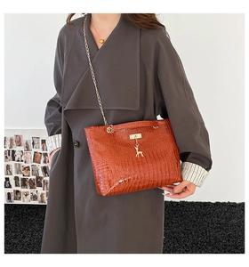 Detail of a brown crocodile texture handbag featuring a gold deer charm and chain strap
