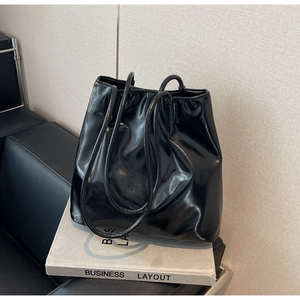 Minimalist black glossy faux leather tote bag with thin round straps on prop book