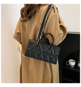 Detail of black quilted handbag with geometric pattern and striped wide shoulder strap