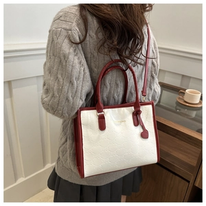 Detail of red and white contrast tote bag featuring bow embossing and heart charm