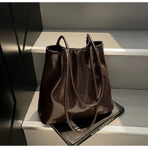 Detail of glossy dark brown faux leather tote bag on steps with fashion magazines