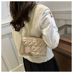 Détail du sac bandoulière beige matelassé avec chaîne dorée et boucle porté par mannequin