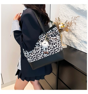 Dettaglio della borsa tote leopardata con base in pelle nera e ciondolo a pompon