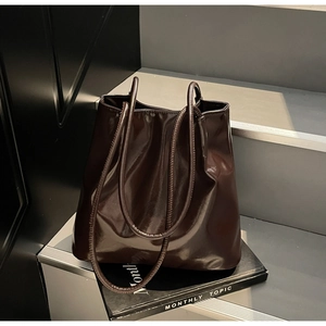 Detail showing the glossy dark brown patent leather texture and slim handle of the tote bag