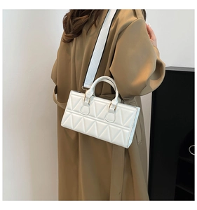 Detailed view of white quilted handbag with wide woven strap on a beige coat