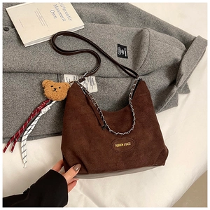 Détail d'un sac hobo en daim marron foncé avec chaîne argentée et breloque ours en peluche