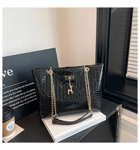 Detail of black faux leather tote with crocodile pattern and golden deer pendant