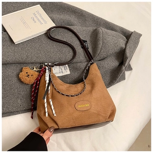 Détail du sac hobo avec breloque ours et chaîne en métal sur fond de manteau en laine