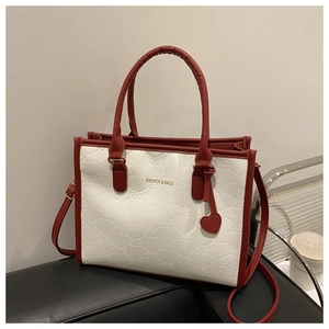Close-up of contrast color tote bag with bow texture, heart pendant, and leather handles