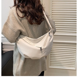 Detailed view of a white textured crescent bag with a wide strap on a model wearing beige