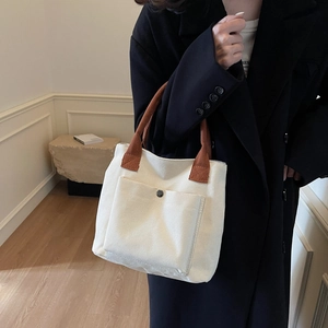 Sac fourre-tout minimaliste en toile blanc cassé avec anses brunes, porté à la main