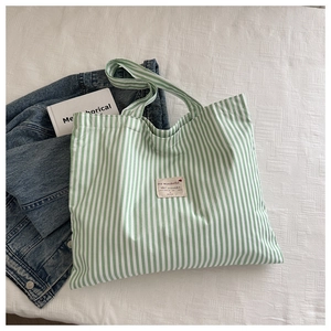 Detailed view of the green striped canvas tote bag with decorative heart label on white fabric