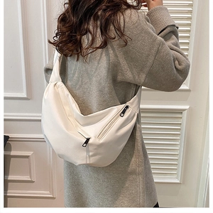 Side view of cream leather crescent crossbody bag shown worn by a model in casual grey sweater