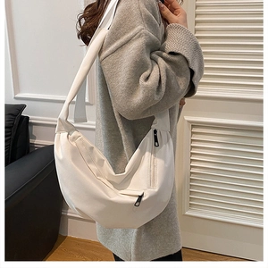 Close-up of a white crescent crossbody bag with black zippers and wide shoulder strap