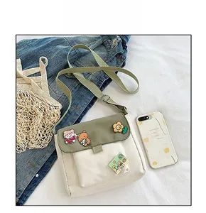 Détail du sac bandoulière en toile avec des badges cartoon et une sangle verte
